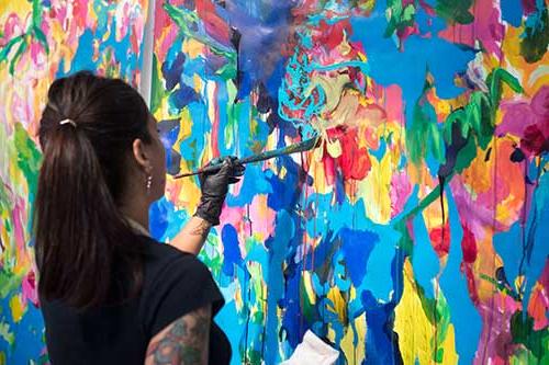 person painting a canvas in an abstract way with variety of bright colors: blue, green, yellow